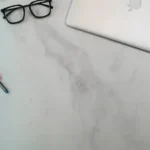 a laptop, pen, ruler, eyeglasses, and pencil on a marble