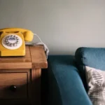 photo of yellow rotary telephone near blue sofa
