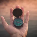 person holding black and green compass pointing to west