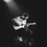 grayscale photo of man playing guitar on stage