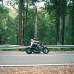 person riding motorcycle passing on road surround by trees