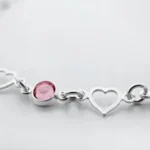 a silver bracelet with three hearts and a pink stone