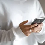 person in white long sleeve shirt holding black smartphone