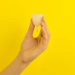a hand holding a piece of food over a yellow background