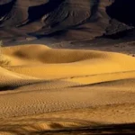 a desert landscape with sand dunes and mountains in the background