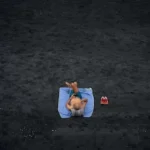 shirtless man lying on blue picnic mat on the field