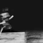 grayscale photo of woman in white shirt and black pants sitting on concrete floor