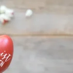 a hand holding a red painted egg with the words cherry is risen written on it