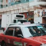 red and white taxi sedan running on road near 7 Eleven store signage