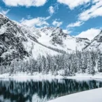 lake near trees and mountain under blue sky during daytime