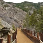 a dirt path with a wooden fence and a mountain in the background