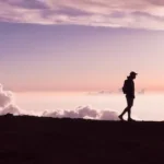 silhouette of person walking under white clouds