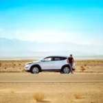 man standing beside white SUV near concrete road under blue sky at daytime