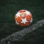white and orange soccer ball on green grass field