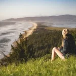 person sitting on hill near ocean during daytime