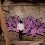 man in white pullover hoodie leaning on purple graffitied wall