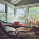 photography of grey, white, and brown wooden house interior with three brown wooden Windsor chairs beside brown hammock with glass windows