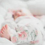 baby in white and red floral onesie lying on bed