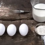 three white eggs beside stainless steel fork and knife on brown wooden table