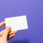 a hand holding a white business card against a purple background