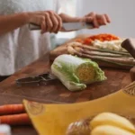 person slicing green vegetable on brown wooden chopping board