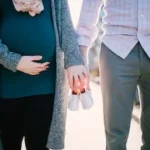 man standing beside pregnant woman holding baby's shoes during daytime
